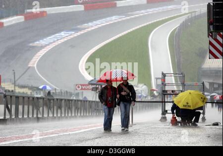 (Dpa) - im strömenden Regen laufen Formel-1-Fans durch die Boxengasse auf die Rennstrecke in Spa-Francorchamps, Belgien, 26. August 2004. Im Hintergrund die berüchtigten Kurve "Eau Rouge" ersichtlich. Am Sonntag 29. August statt findet auf dem Golfplatz die Formel 1 Rennstrecke in Belgien. Stockfoto