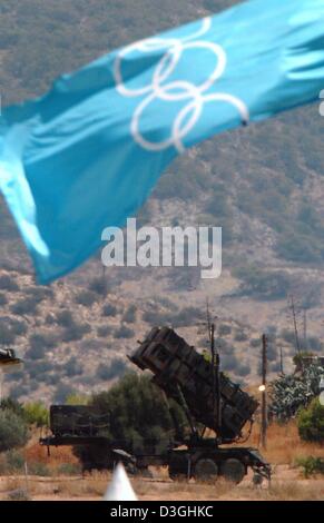 (Dpa) - die Olympische Flagge Wellen vor ein Patriot Flugabwehrraketen Batterie steht auf Stand-by-als Teil der Sicherheitsmaßnahmen für die Olympischen Spiele 2004 in der Nähe von Helliniko Olympic Complex in Athen, 30. Juli 2004. Stockfoto