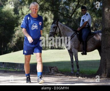 (Dpa) - Morten Olsen, Fußball-Trainer der dänischen Fußball-Nationalmannschaft geht vorbei an einem montierten portugiesischen Polizeibeamten in Alvor, Portugal, Freitag, 25. Juni 2004. Dänemark wird gegen die Tschechische Republik in das Endspiel der Fußball EM 2004 Quartal auf Sonntag, 27. Juni 2004 zu spielen. Stockfoto