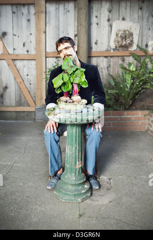 Hipster und Beatniks - ein Junge Hipster-Mann mit Schnurrbart und Brille noch essen Rüben auf gepflanzt ein Vogelbad in seinem eigenen Garten Stockfoto