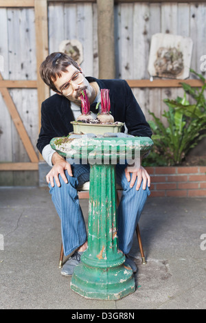 Hipster und Beatniks - ein Junge Hipster-Mann mit Schnurrbart und Brille noch essen Rüben auf gepflanzt ein Vogelbad in seinem eigenen Garten Stockfoto