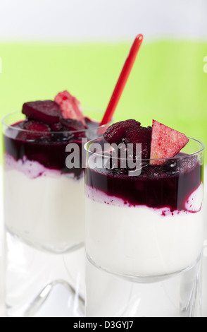 Zwei Gläser hausgemachte Joghurt Quark Dessert mit Heidelbeeren und Apfelscheiben auf grünem Hintergrund Stockfoto