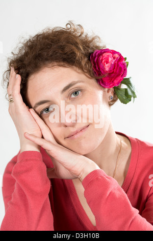 junge lockig Frau trägt Rosa Kleidung und rote Blume im Haar Stockfoto