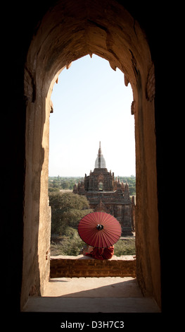 Junge Novize und Sonnenschirm, gerahmt in einem Torbogen Bagan-Tempel. Stockfoto