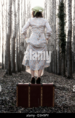 eine Frau in einem floralen Vintage Kleid steht auf einem alten Koffer Stockfoto