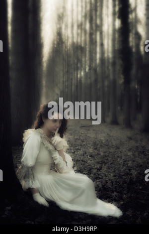 eine Frau in einem viktorianischen Kleid sitzt in den Wäldern, die ein Geheimnis Stockfoto
