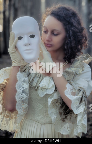 eine Frau in einem Zeitraum Kleid hält eine weiße Maske Stockfoto