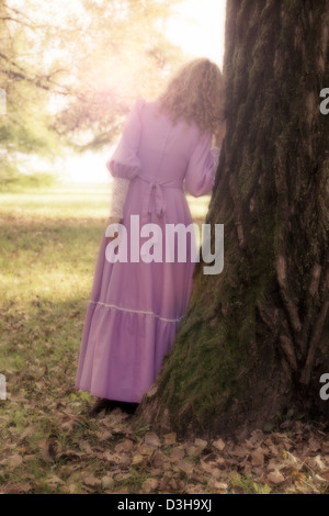 eine Frau in einem rosa Kleid ist gegen einen Baumstamm gelehnt. Stockfoto