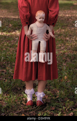 eine Frau in einem roten Kleid mit einer alten Puppe Stockfoto