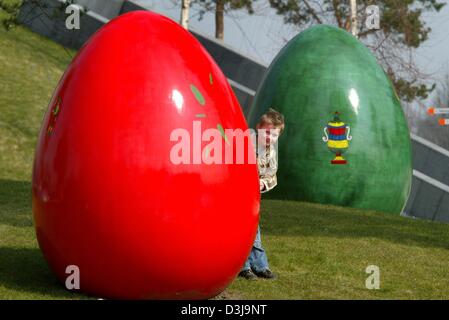 (Dpa) - späht wenig Niklas heraus von hinten ein Riesen Osterei in Wolfsburg, Deutschland, 1. April 2004. 41 bunte Eiern wurden auf dem Gelände VWs "Autostadt" (Autostadt) zu seinen Gästen in einer frühen Oster-Stimmung zu kommen. Stockfoto