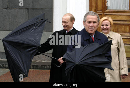 (Dpa) - US-Präsident George W. Bush und der russische Präsident Wladimir Putin (L) kämpfen mit Thieer Schirme als Putins Frau Ludmila blickt auf und lächelt während der Feierlichkeiten anlässlich des 60. Jahrestages des Endes des zweiten Weltkrieges in Moskau, Russland, Montag, 9. Mai 2005. Russland feiert mit zahlreichen eingeladenen Staaten Sieg den Alliierten über Nazideutschland. Stockfoto