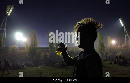 (Dpa) - steht ein Punk mit einem Plastikbecher Bier leicht beleuchtet in der Mauer Park in Berlin, Deutschland, 30. April 2005. Im Hintergrund Parken die Flut Lichtmasten des Friedrich-Jahn-Sport Stadion. Am Vorabend des Mai-Tag in der Regel rock Stein lobbing Jugendliche der Stadt Berlin. Nur die Ausschreitungen in diesem Jahr war kleiner skaliert und Polizei hatte eine fast friedliche Arbeit. Stockfoto