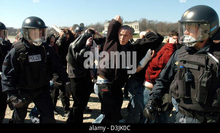 (Dpa) - Polizisten (L, R) in Kampfmontur bewachen die Teilnehmer von einer Kundgebung von Neonazis in München, Deutschland, 2. April 2005. Wütende Demonstranten warfen Flaschen und Dosen auf die Rechtsextremisten. 300 Personen nahmen an der Neonazi-Kundgebung während 6.000 Leute schlossen sich den Protesten gegen die Kundgebung. Stockfoto