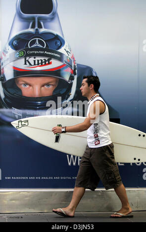 (Dpa) - verweilt Robbie ein Surfer mit seinem Surfbrett vorbei ein Werbeplakat mit dem Bild des finnischen Formel-1 pilot Kimi Raeikkoenen von McLaren-Mercedes in Melbourne, Australien, Dienstag, 1. März 2005. Das erste Rennen der 2005 Formel-1-Saison, den Australian Grand Prix startet am Sonntag. Stockfoto