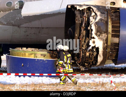 (Dpa) - Feuerwehr vorbeigehen ein abgebranntes Motor für einen Atlas Air Frachtflugzeuge, die hinter der Landebahn am Flughafen in Düsseldorf, 24. Januar 2005. Das Flugzeug rollte weiter als die Start-und Landebahn, nach der Landung und zwei Motoren gefangen Feuer. Das Feuer war schnell löschte und niemand wurde verletzt nach ersten Erkenntnissen. Die Maschine kam aus Dubai. Stockfoto