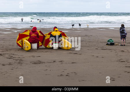 RNLI Rettungsschwimmer und einen kleinen Jungen Schutz vor dem kalten Wind auf der Black Rock Beach, Widemouth Bay, Nr. Bude, Cornwall, UK Stockfoto