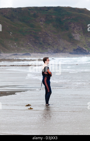 Ein junger Mann steht und sieht Surfer auf der Black Rock Beach, Widemouth Bay, Nr. Bude, Cornwall, UK Stockfoto