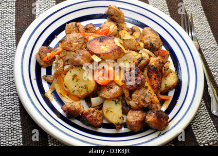 Gebratene Wurst und Kartoffeln serviert auf einem weißen und blauen Teller Stockfoto