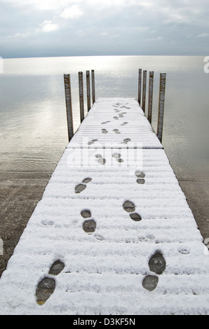 Menschliche Fußspuren im Schnee auf einem Dock führt hin und zurück, auf einem großen großen See. Stockfoto