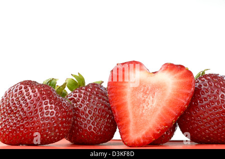 Sehen Sie vier Erdbeeren, einer von ihnen in zwei Hälften geschnitten und mit einer Herzform. Stockfoto