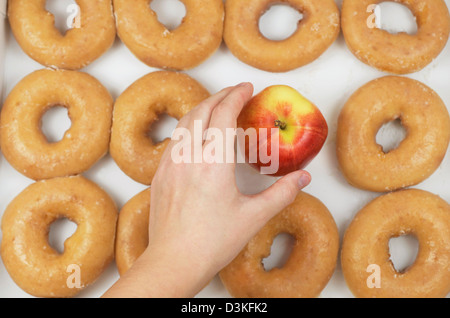 Hand einen Apfel aus der Mitte von einem Dutzend glasierte Donuts in einer Box zu wählen. Stockfoto