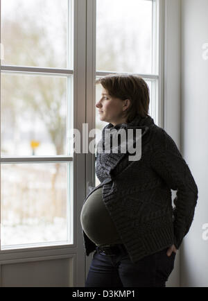 Junge schwangere Frau, 35 Jahre, 9. Monat der Schwangerschaft, Blick aus dem Fenster. Stockfoto