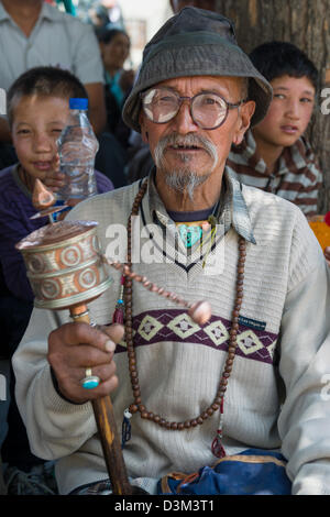 Ältere männliche Pilger tragen eine Gebetsmühle mit zwei jungen über seine Schulter auf einem Festival in Soma Gompa, Leh (Ladakh) Jammu & Kaschmir, Indien Stockfoto