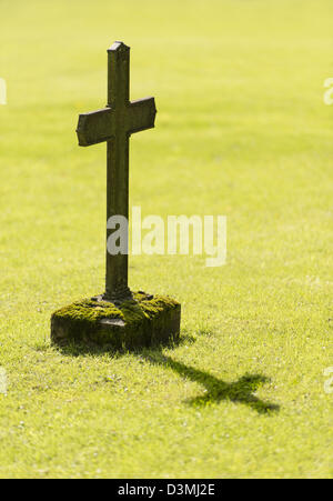 Altes Grab mit christlichen Kreuz wirft einen Schatten auf dem Rasen des Friedhofs Stockfoto