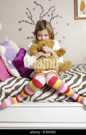9 Jahre altes Mädchen sitzt auf ihrem Bett umarmt einen Teddybär Stockfoto