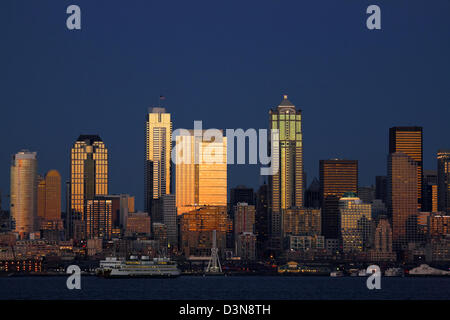 Die Hochhäuser der Innenstadt von Seattle und die Uferpromenade, darunter das Great Wheel und eine Cross-Sound-Fähre, in der Elliot Bay in der Abenddämmerung. 2012 Stockfoto