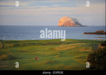 Zwei Golfer gehen Sie das Fairway auf North Berwick Golf Club, wie die Sonne über Bass Rock in den Firth of Forth in Schottland. Stockfoto