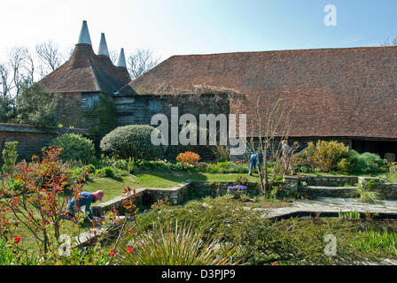 Great Dixter House und Gärten, blauer Frühling, Himmel Tulpen und Sträucher gegen historische große Scheune und Oast House. Bunte Stockfoto