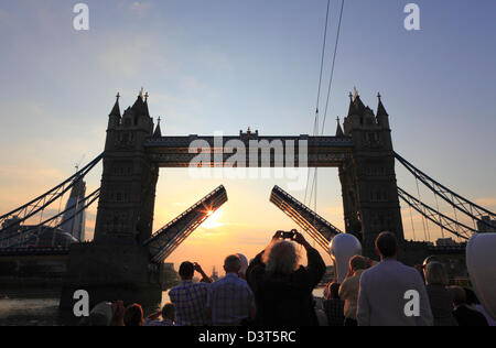 Touristen fotografieren die Tower Bridge, die für ihr Boot aufgezogen wurde, um durch die Brücke zu fahren, bei Sonnenuntergang von einem Boot auf der Themse London England GB. Stockfoto
