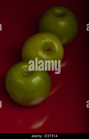 Grüne Äpfel (Granny Smith) auf rotem Grund Stockfoto