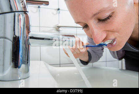 Frau ist ihre Zähne putzen, solange Wasser aus dem Wasserhahn läuft. Symbol-Bild für Wasserverschwendung. Stockfoto