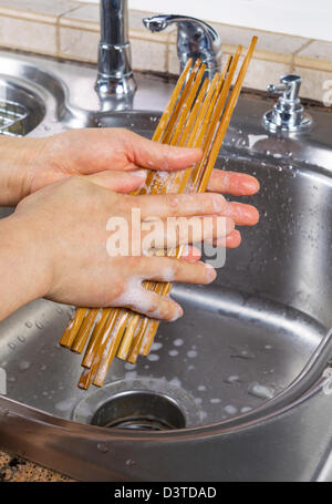 Vertikale Foto von weiblichen Händen Reinigung Bambus Stäbchen mit Seifenwasser zusammen mit Spüle und Wasserhahn im Hintergrund Stockfoto