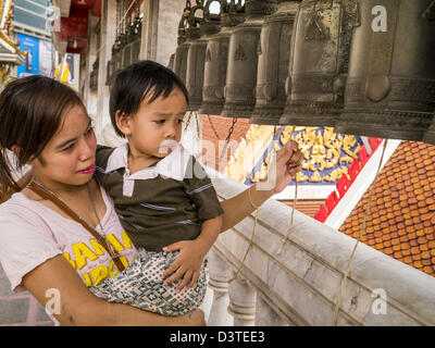 24. Februar 2013 Ringe - Bangkok, Thailand - eine Frau mit ihrem Kind Gebet Glocken an Wat Hua Lamphong. Wat Hua Lamphong ist ein Royal buddhistischer Tempel, dritte Klasse, in der Bang Rak Viertel von Bangkok, Thailand. Es befindet sich an der Rama IV Road, etwa 1 km von der Stadt Hua Lamphong Hauptbahnhof. Ein Eingang zu Sam Yan Station auf der Bangkok Metro (u-Bahn) befindet sich vor dem Haupteingang des Tempels Verbindung auf Rama IV. Wat Hua Lamphong wurde 1996 anlässlich des 50. Jahrestages der Aufstieg auf den Thron von König Bhumibol Adulyadej (Rama IX) im Jahr 1996 renoviert. Das königliche Siegel o Stockfoto