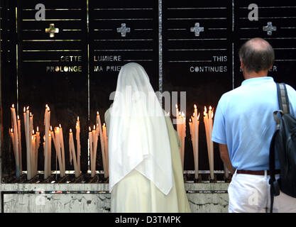 (Dpa-Datei) - eine Nonne mit einem weißen Schleier und ein Pilger stehen vor einer Nische mit brennenden Kerzen in den Wallfahrtsort Lourdes, Frankreich, 8. September 2006. Am 11. Februar 1858 14-jährigen Bernadette Soubirous hatte Visionen von der Jungfrau Maria in der Grotte Massabielle in der Nähe des Flusses Gave du Pau wiederholt. Während einer dieser Visionen entdeckt Berrnadette der Grotte dessen Wasser Stockfoto