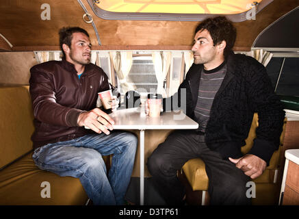 Zwei Surfer sitzen am Tisch im VW Campervan, St. Agnes, Cornwall, UK Stockfoto