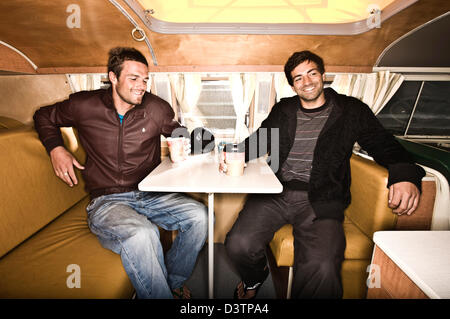 Zwei Surfer sitzen am Tisch im VW Campervan, St. Agnes, Cornwall, UK Stockfoto