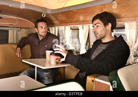 Zwei Surfer sitzen am Tisch im VW Campervan, St. Agnes, Cornwall, UK Stockfoto