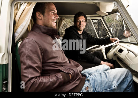 Zwei Freunde sitzen lachend in VW Campervan, St. Agnes, Cornwall, UK Stockfoto