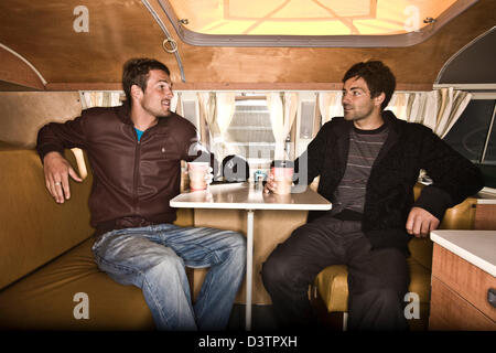 Zwei Surfer sitzen am Tisch im VW Campervan, St. Agnes, Cornwall, UK Stockfoto