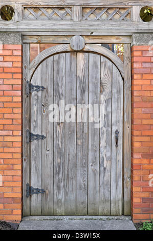 Holztür mit abgerundeten Spitze in Mauer nahe, ein Gartentor geschlossen und verriegelt. Stockfoto