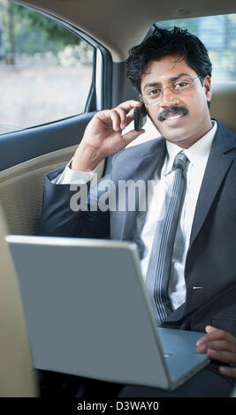 Südindische Geschäftsmann mit einem Laptop und sprechen auf einem Handy im Auto Stockfoto