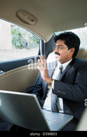 Südindische Geschäftsmann Blick durch das Fenster eines Autos und winkenden hand Stockfoto