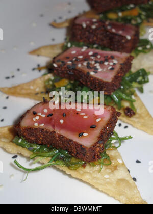 Essen - Sesam und fast Käserand gebratene Ahi Thunfisch Fischgericht.  Sesam bedeckt Thunfisch-Scheiben auf Cracker und Greens. Stockfoto