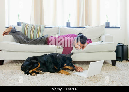 Eine lässige Hispanic-Latino Jüngling unterhaltsam sein Haustier Hund surfen Internet mit Laptop Stockfoto