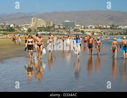 Gruppe von Menschen zu Fuß auf dem nassen Sand am Playa del Inglés, Gran Canaria Stockfoto