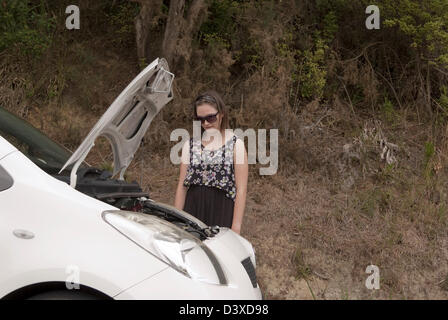 Eine junge Frau sieht ihr Auto bei geöffneter Motorhaube besorgt. Stockfoto